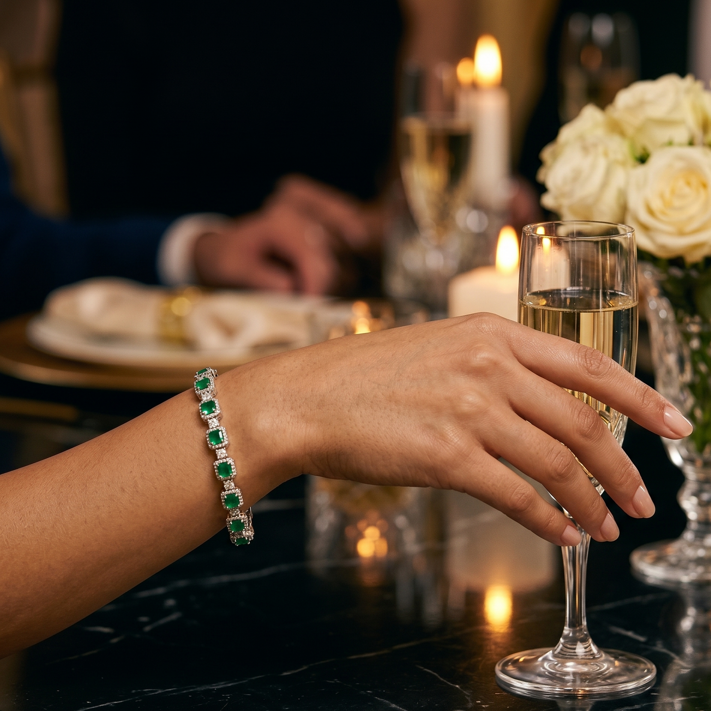 Hand holding a glass of champagne with a bracelet on a dinner table setting.